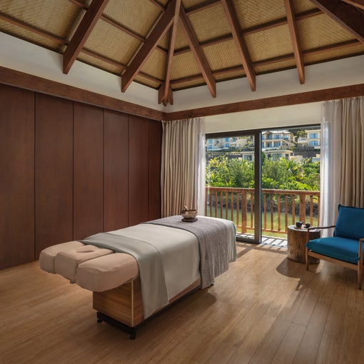 Thermal suite featuring massage table, durable wood flooring, large windows overlooking garden, blue chair and abundant natural light.