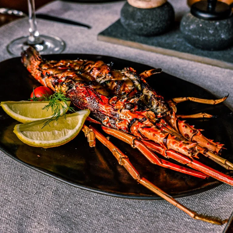 龙虾装在黑色盘子里,配以柠檬片、樱桃番茄和莳萝装饰,铺在灰色桌布上。.