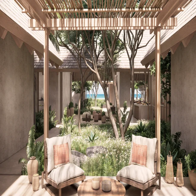 Lounge area featuring cushioned seating under a wooden pergola, surrounded by greenery and overlooking a courtyard with trees and pathway to the shore.