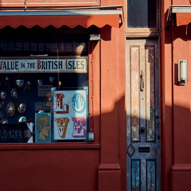 A wooden door and window set in a warm reddish-orange wall, displaying colorful “LOVE” letters and circular mirrors, illuminated by natural light.