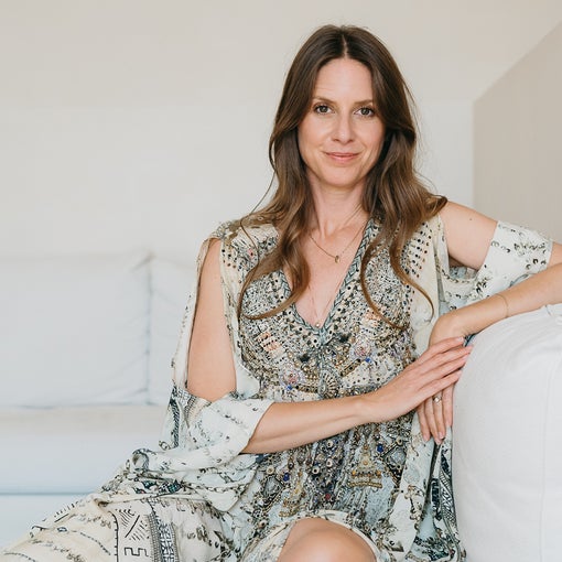 Person wearing a patterned dress sits on a white sofa, smiling softly in a bright, minimalist space with natural light.