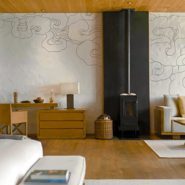 起居室内有天然木质家具、环保炉灶、带有宁静云朵图案的白色墙壁以及黄色坐垫的舒适沙发。.