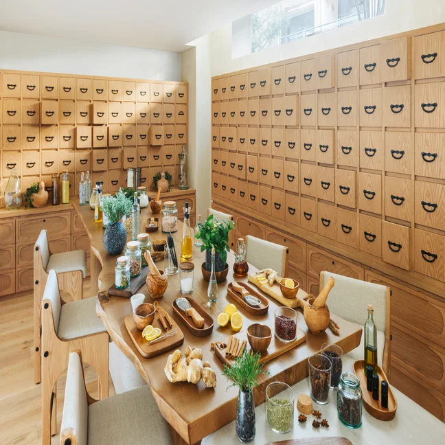 Spacious room featuring wood cabinetry and a large table arranged with herbs, spices, glass bottles, and kitchen essentials for holistic wellness experiences.