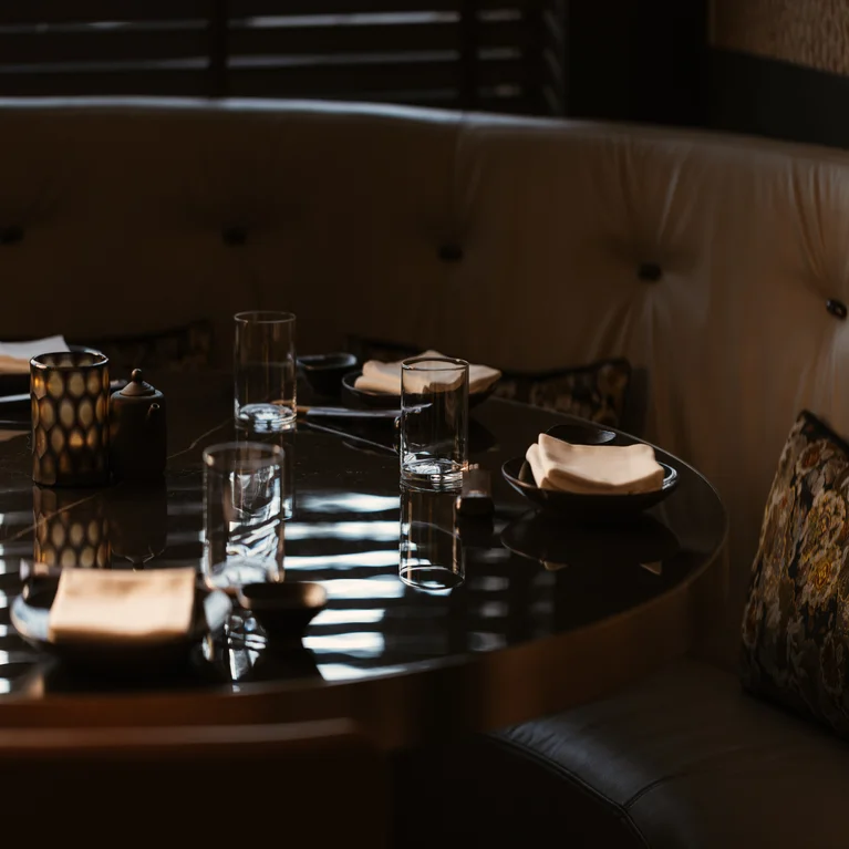 A circular dining table set with glasses and small plates, framed by a curved leather booth.