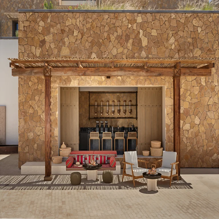 Sustainable pergola shades a lounge with soft seating, natural materials, and a discreet bar, blending indoor comfort with mindful outdoor design.