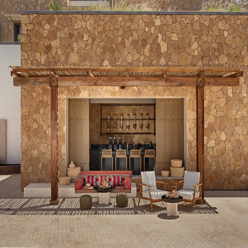 Sustainable pergola shades a lounge with soft seating, natural materials, and a discreet bar, blending indoor comfort with mindful outdoor design.