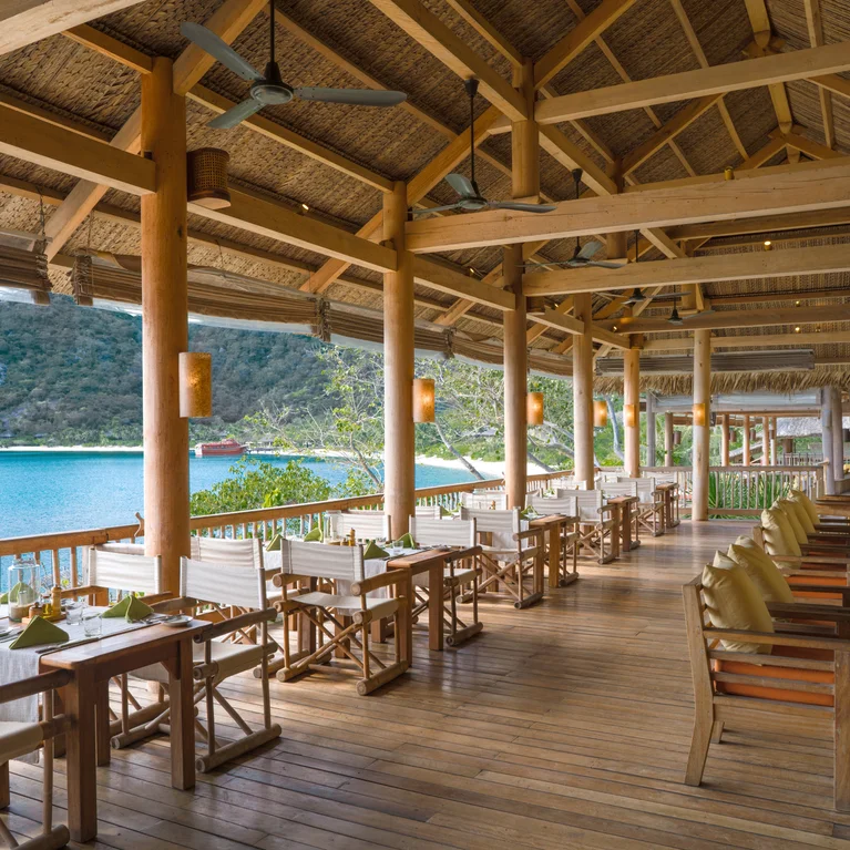 Restaurant with natural timber features, spacious tables and chairs, offering views of a tranquil lake and forested hills in the background.