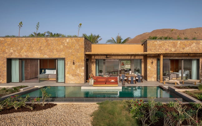 Stone villa featuring large glass doors, shaded outdoor lounge, private pool, native gardens, and surrounding mountain views. Designed for comfort and sustainable living.