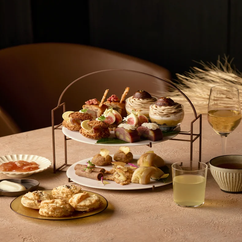 ペストリーやスライスしたイチジク、小さなケーキが盛られた2段のスタンドに、スコーン、ジャム、そして紅茶が添えられている。.