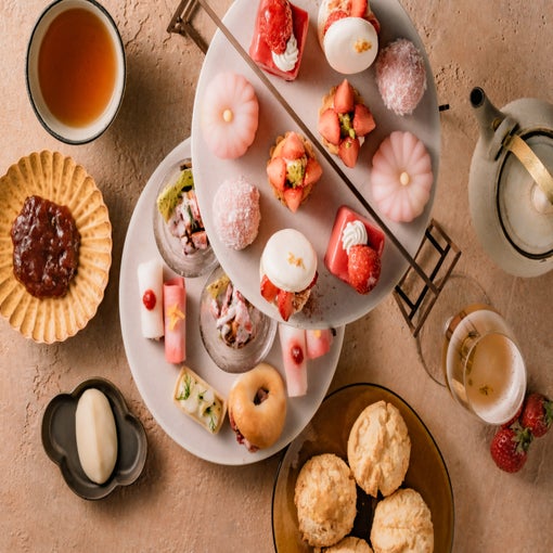 マカロン、スコーン、餅など、芸術的に盛り付けられたデザートが、陶器の皿と急須に盛られたお茶とともに、ナチュラルな色調のテーブルの上に供される。.