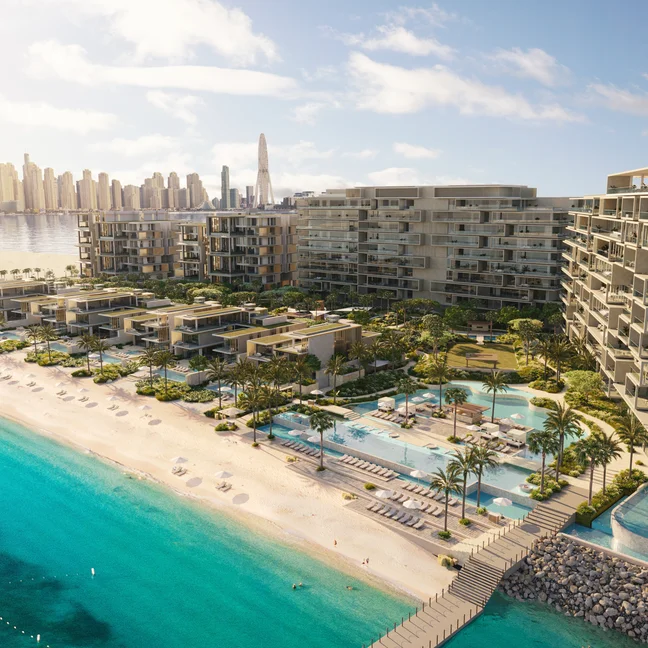 Resort with pools, shaded palm trees, and lounge seating beside clear turquoise waters; city skyline visible in the distance beneath a bright sky.